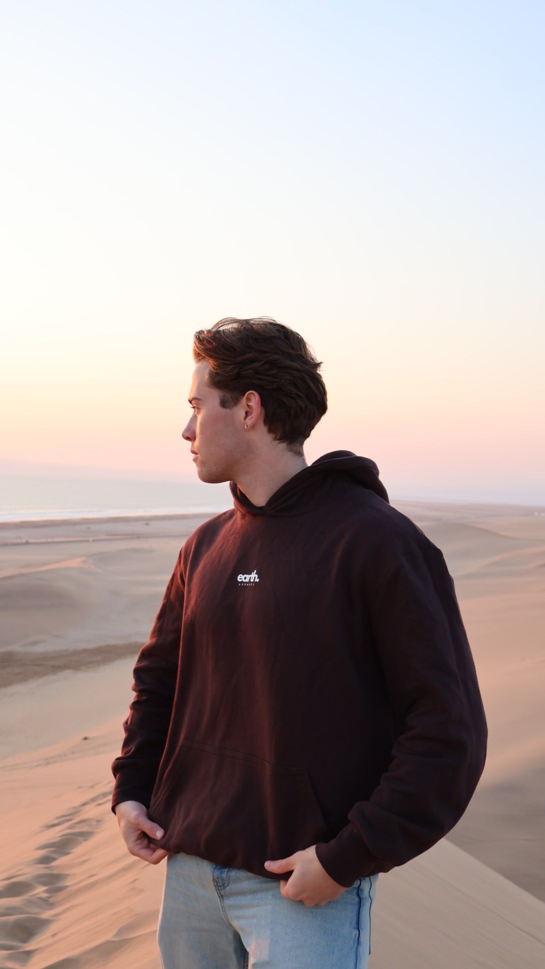 Person wearing a brown hoodie with a logo, standing against a neutral background