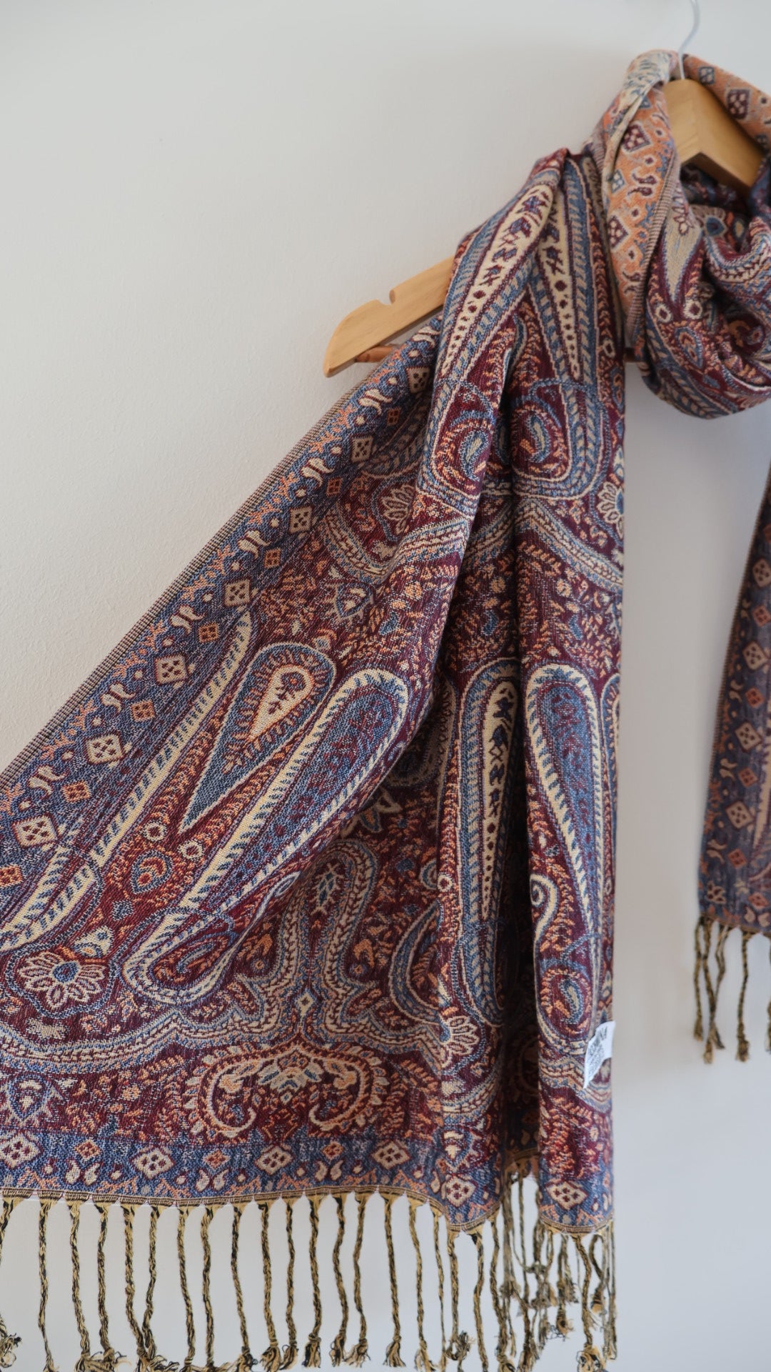 Maroon blue boho festival pashmina scarf draped on a hanger, side one.
