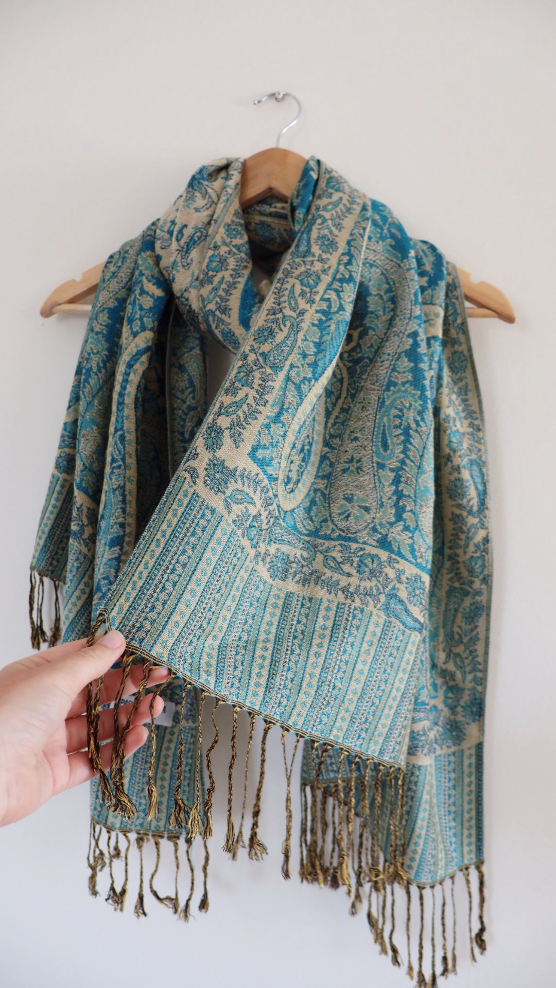 Turquoise boho festival pashmina scarf draped on a hanger, side 1.