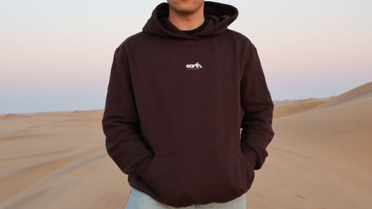 Person wearing a brown hoodie with 'earth' logo in a desert setting