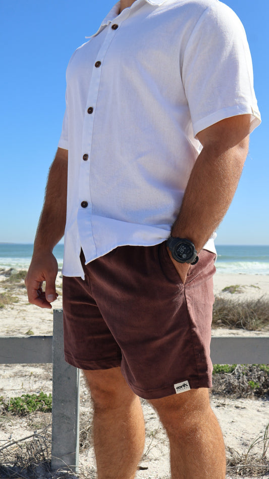 Men's corduroy shorts in earthy tones on model with visible texture, side pockets and elasticated waistband with drawstring.