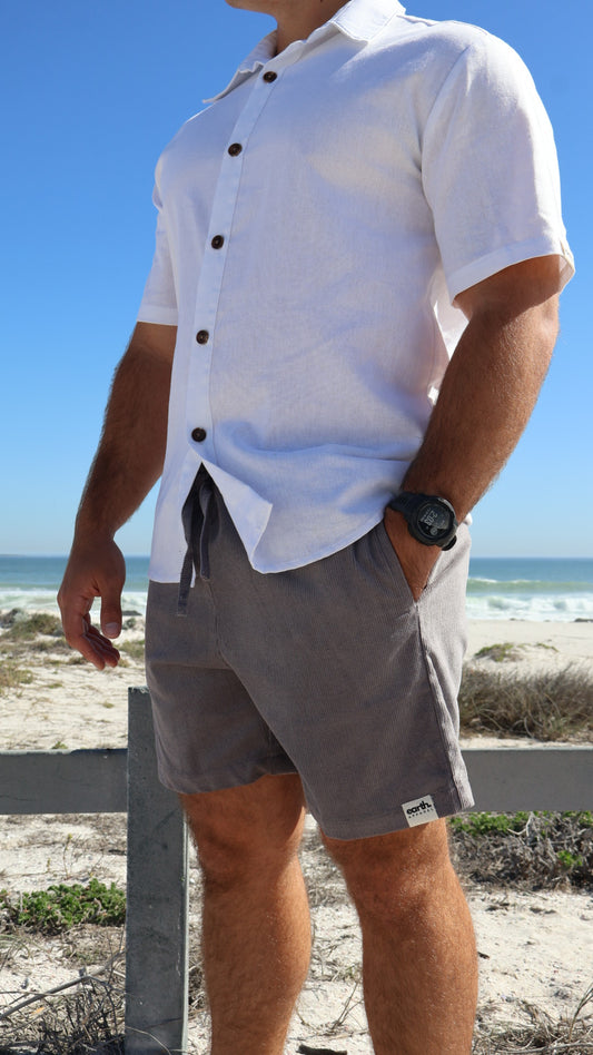 Men's corduroy shorts in earthy tones on model with visible texture, side pockets and elasticated waistband with drawstring.