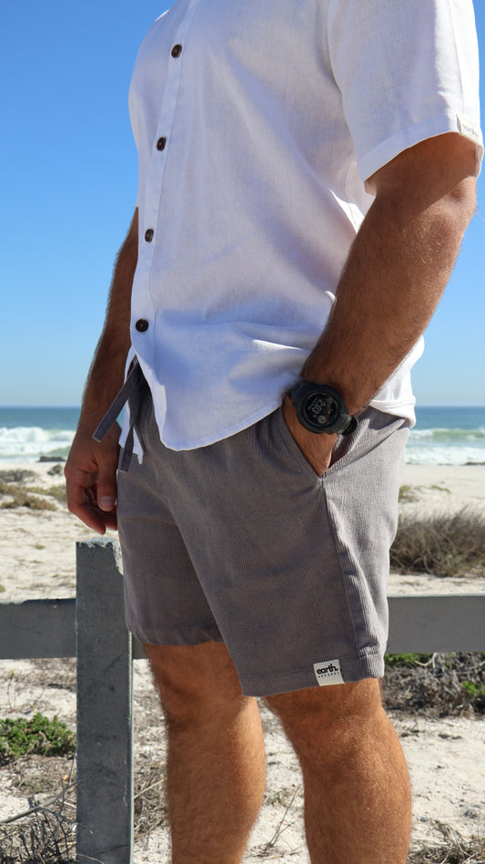 Men's corduroy shorts in earthy tones on model with visible texture, side pockets and elasticated waistband with drawstring.