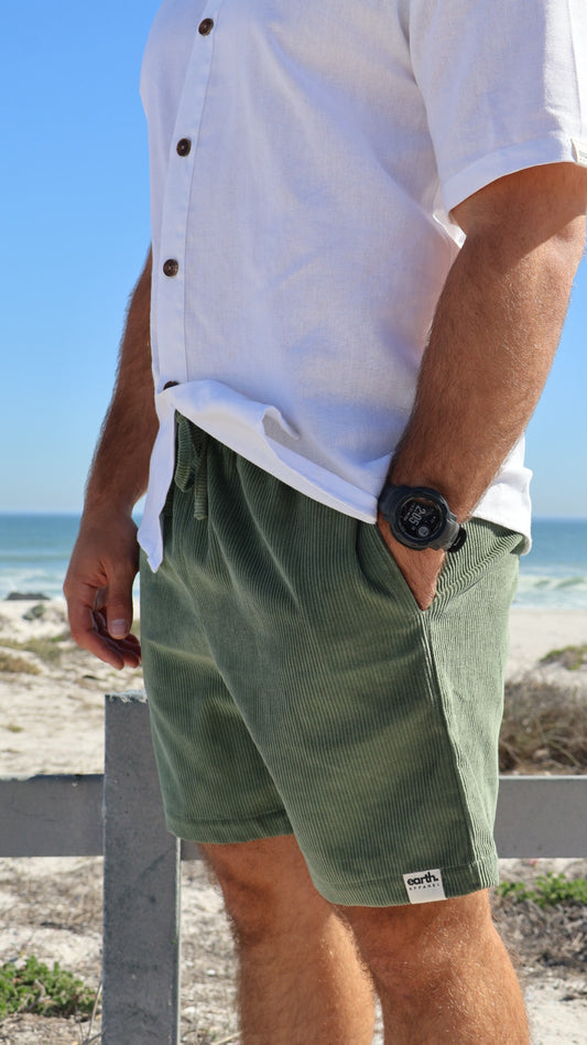 Men's corduroy shorts in earthy tones on model with visible texture, side pockets and elasticated waistband with drawstring.