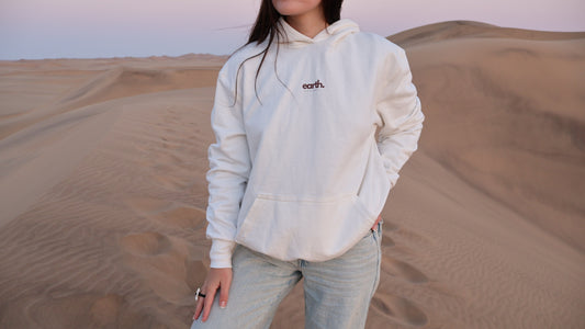 Person wearing a light-colored hoodie with 'earth' logo in a desert setting
